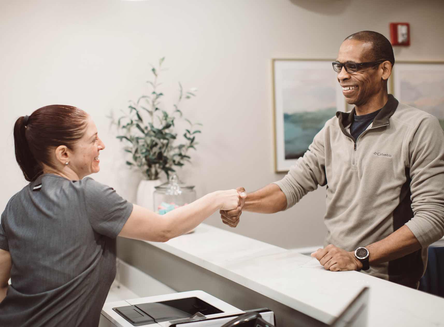Photo of a Woodside team member shaking hands at the front desk with a patient